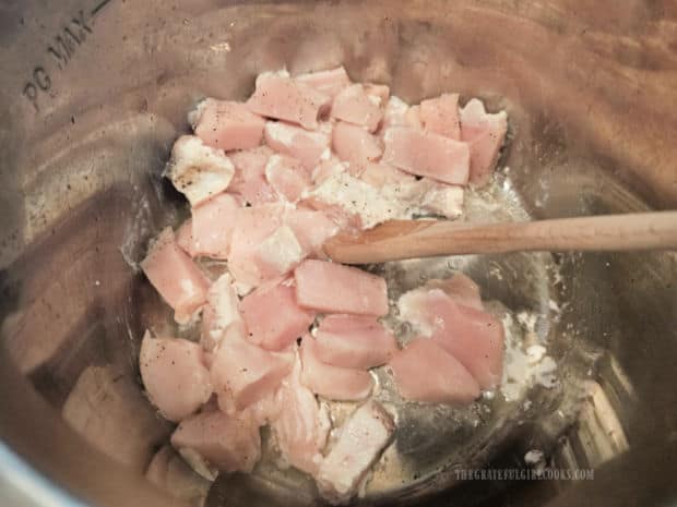 Olive oil is heated in Instant Pot and chicken chunks are added.