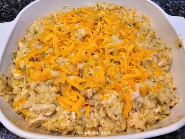 Cheesy chicken rice casserole is transferred to baking dish and topped with more cheese.
