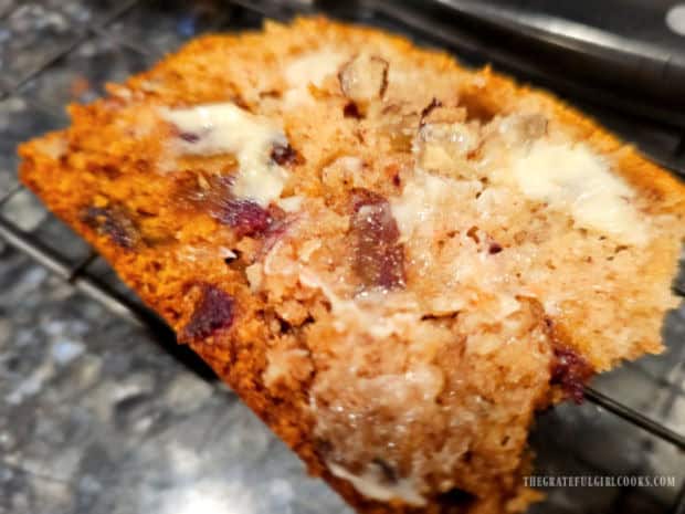 Soft butter is spread on a warm slice of date nut bread.