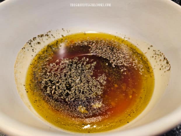 Spices and minced garlic are added to the oil and vinegar in bowl.