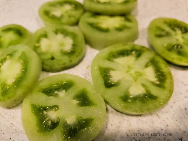 Unripe, firm green tomatoes are rinsed, de-stemmed, and sliced into rounds.