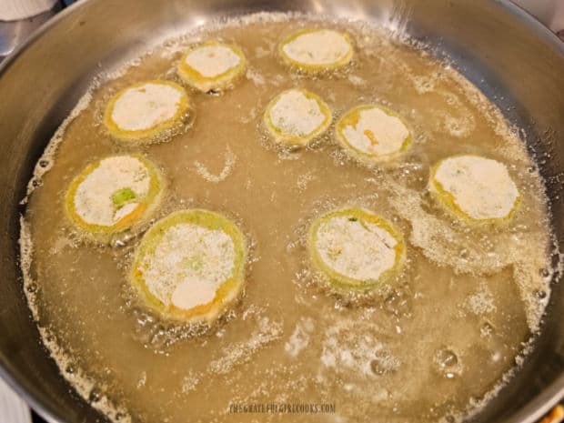 Fried green tomatoes are cooked in hot oil, flipping them over, halfway through frying time.