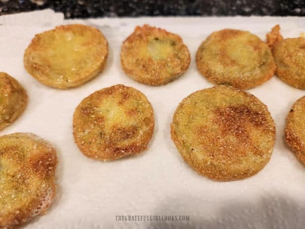 After frying, the tomato slices drain on paper towels before serving.