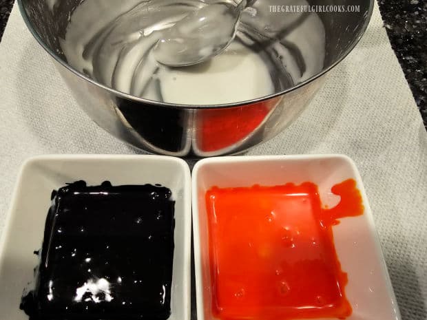 A bowl of white icing, and 2 small bowls of black and orange icing.