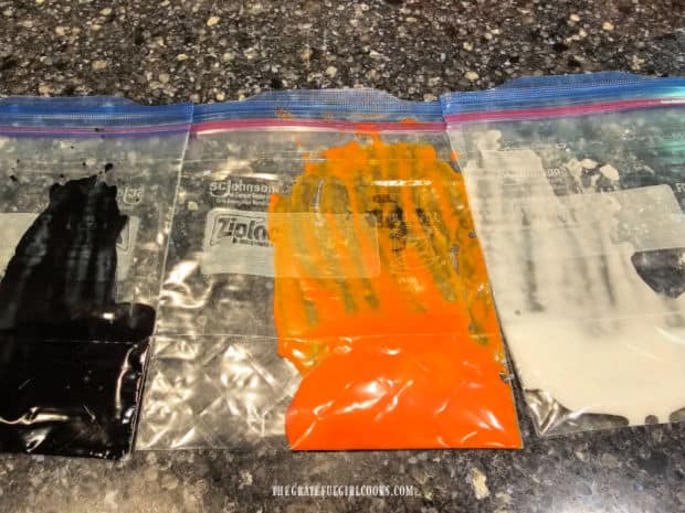 Three bags holding black, orange and white icing for homemade decorative sprinkles.
