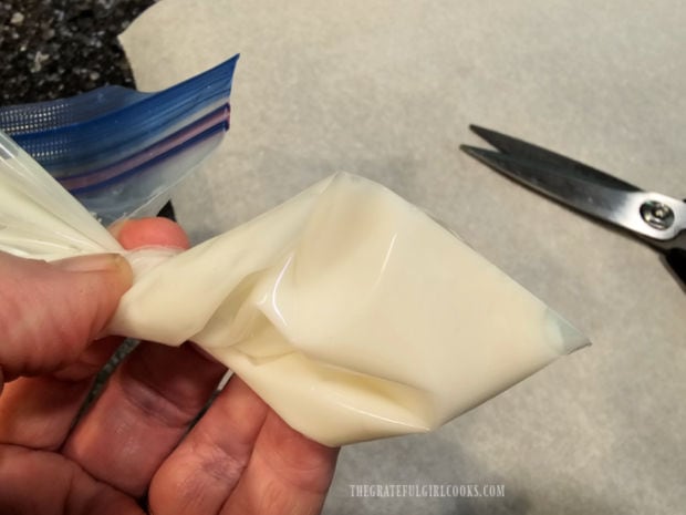 A small cut is made in the corner of a piping bag filled with white icing.