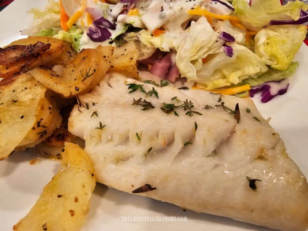 A white plate with baked cod and potatoes, served with a green salad on the side.