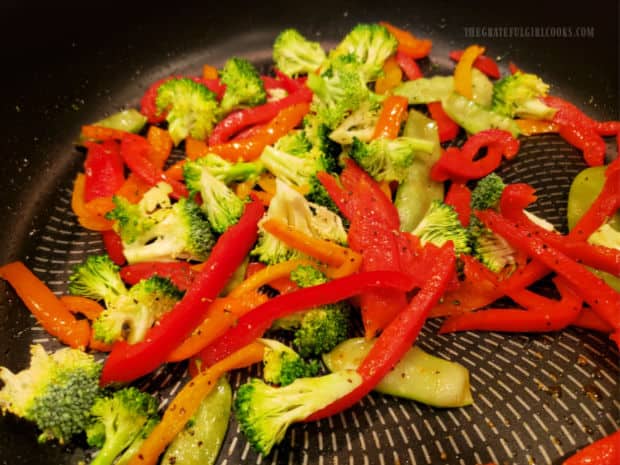 Broccoli, snap peas, red and orange bell peppers are stir-fried in skillet.