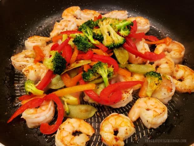 Stir-fried veggies are added to the cooked shrimp in the skillet.