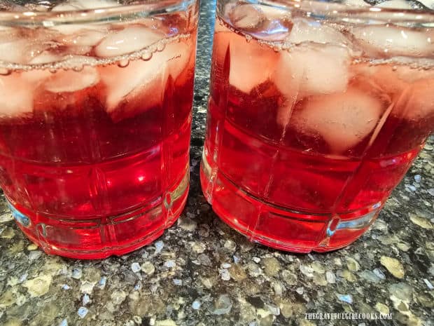 Two glasses of apple cranberry juice, served over ice cubes.