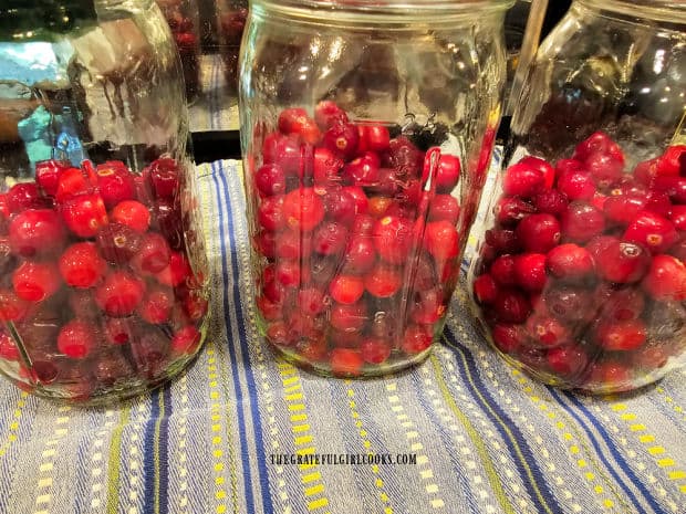 Fresh cranberries are added to three quart-sized canning jars.