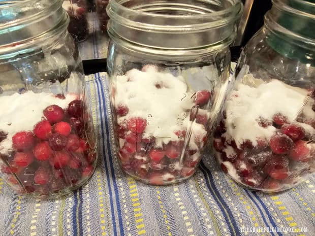 Granulated sugar is added to the cranberries in the quart-sized canning jars.