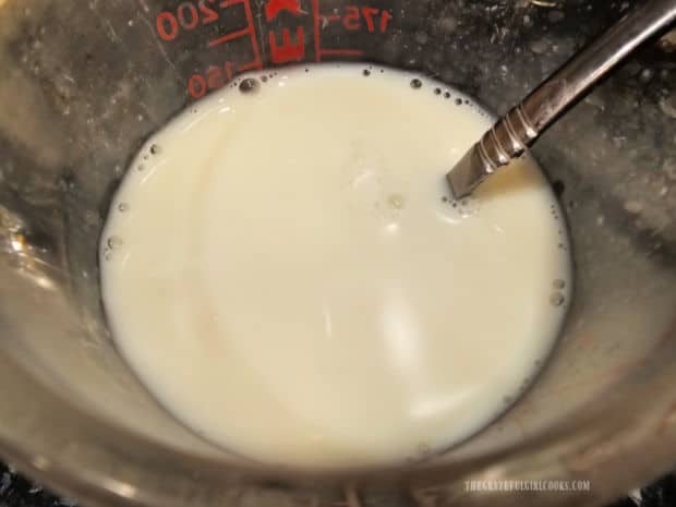 Milk is mixed with hot sauce and yellow mustard in a measuring cup.