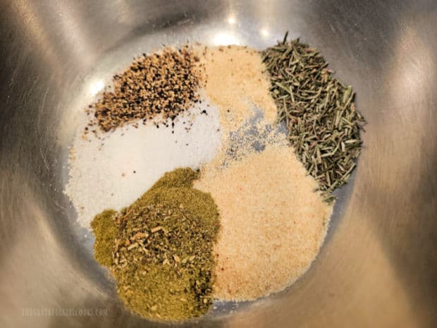 A variety of dried spices are measured into a small bowl.