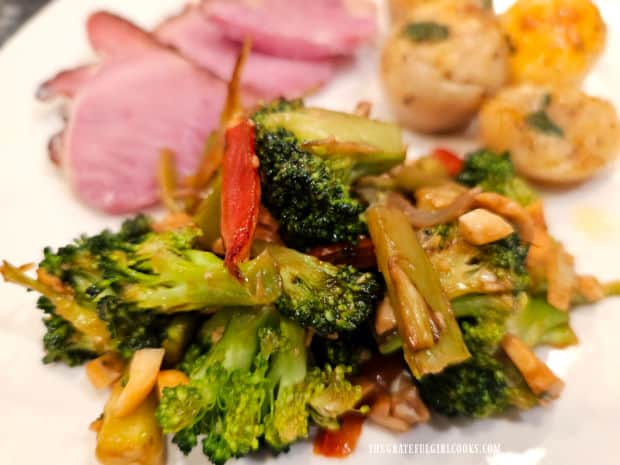 A white plate with broccoli cashew stir-fry, and ham and potatoes in the background.