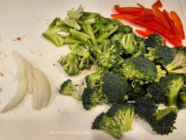 Broccoli florets, stems, sliced red bell peppers and onions are prepped before cooking.