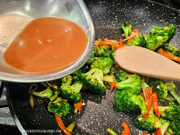 Sauce is poured into the skillet full of cooked broccoli, onions and red bell peppers.