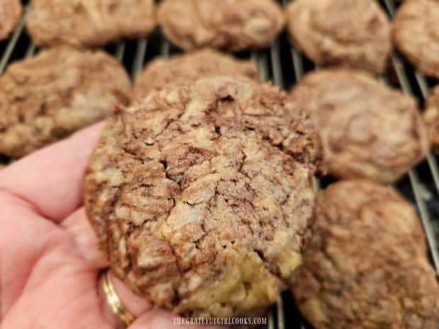 One of the chocolate swirl cookies being held over the wire rack full of the remaining cookies.