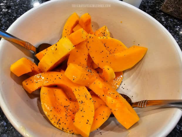 Butternut squash slices are tossed with olive oil, salt and pepper in a bowl.