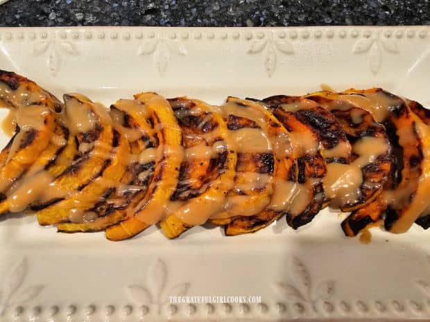 Tahini dressing is drizzled over the top of baked butternut squash slices on platter.