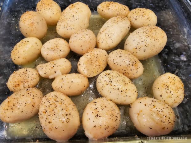 Seasoning salt and garlic powder are sprinkled on the butter-covered potatoes.