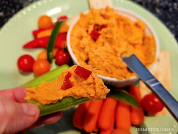 A piece of crunchy celery is used to scoop the roasted red pepper hummus.