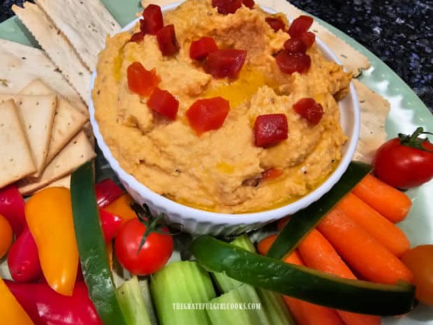 Roasted red pepper hummus is topped with olive oil and more roasted red peppers for garnish.