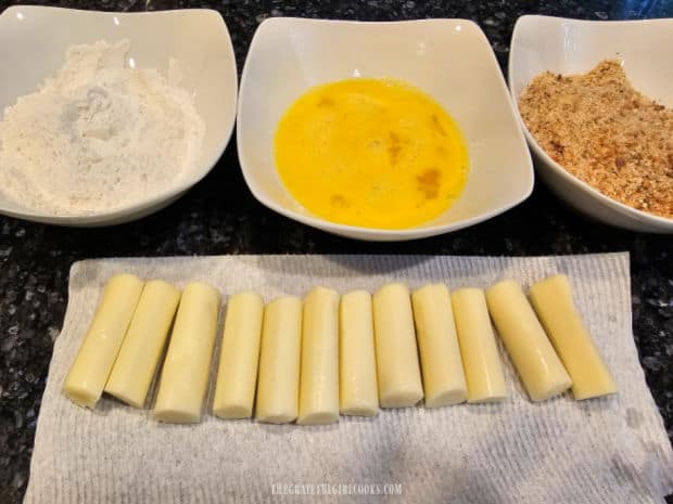 Mozzarella halves ready with three bowls of breading ingredients.