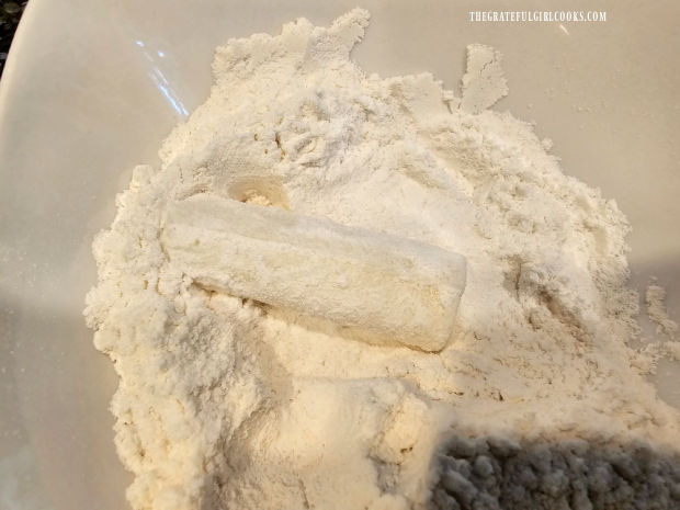A stick of mozzarella string cheese is rolled in a flour mixture until coated.