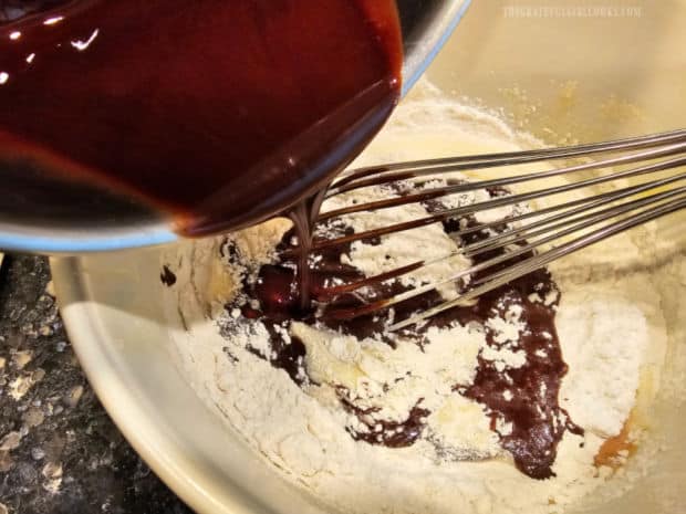 Cooled chocolate mixture is poured over sugar, flour, eggs, etc. in a bowl.