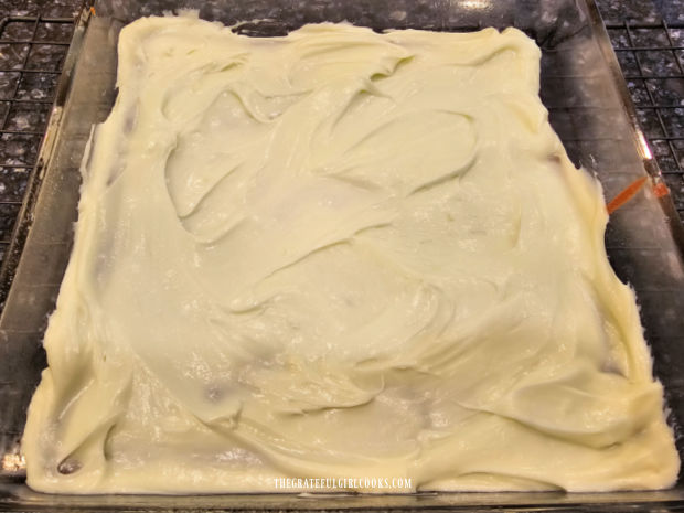 A layer of mint filling is spread over the brownie layer in the baking dish.