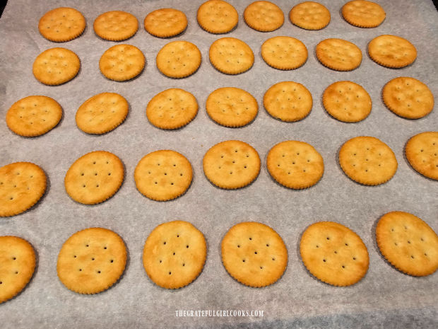 Buttery cracks are spread out in a single layer on parchment paper lined baking sheet.