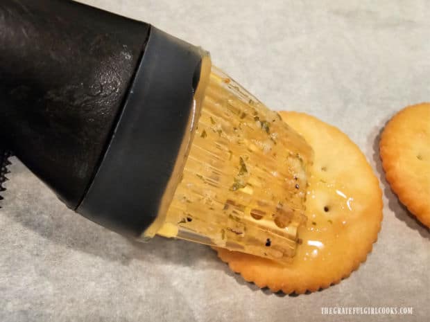 A pastry brush is used to spread the seasoning sauce over top of each cracker.