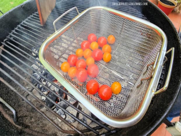 A metal basket holds the cherry tomatoes directly over the hot coals of the BBQ.