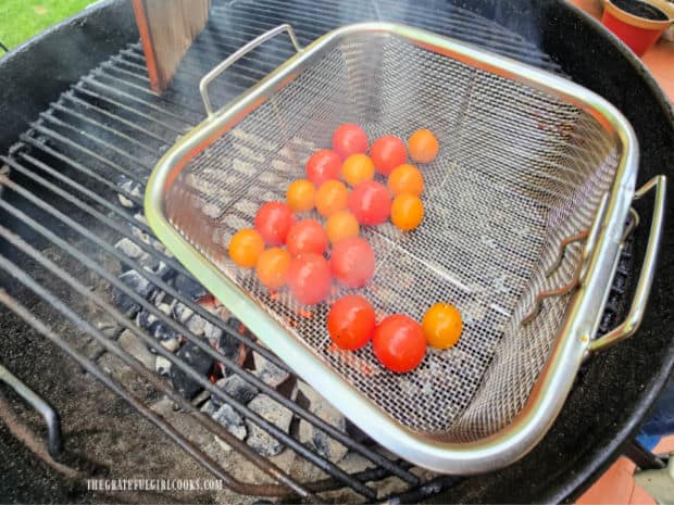 Cherry tomatoes are grilled in a wire basket over hot BBQ coals.
