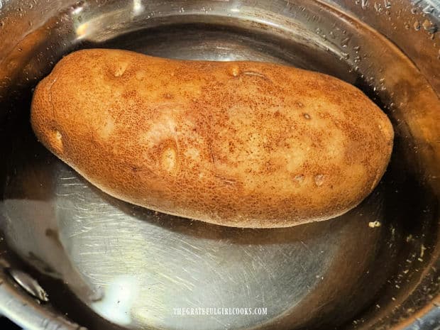 A large potato is boiled until tender in water in a saucepan.