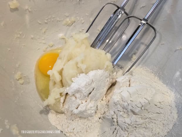 An egg and flour are beaten into the mashed potato in a bowl.