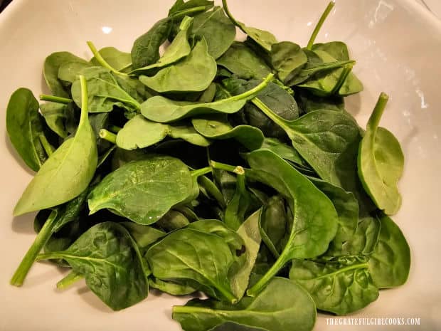 Baby spinach leaves are placed in a large serving bowl.