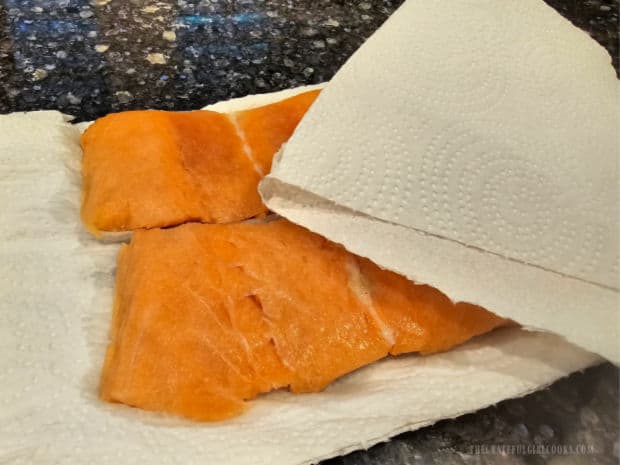 Two thin salmon fillets are patted dry using a paper towel.