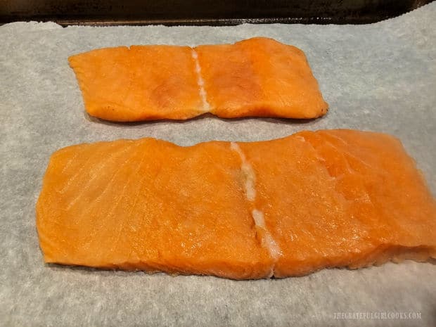 Two salmon fillets are placed on a parchment paper-lined baking sheet.