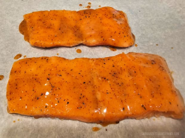 Two skinless salmon fillets are covered with a honey Dijon seasoning sauce before broiling.