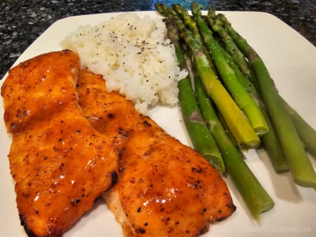 Two pieces of broiled honey Dijon salmon shown on a plate with rice and asparagus.