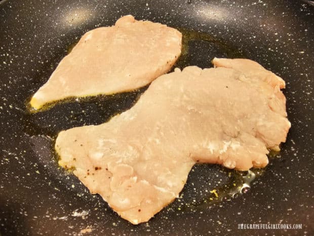 A couple of seasoned, floured chicken breasts cooking in hot oil in skillet.