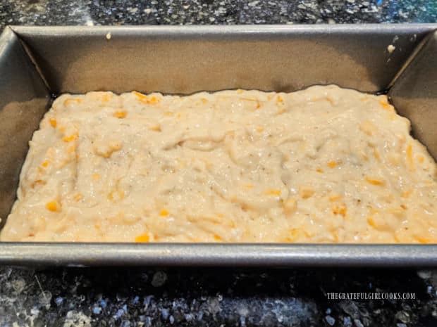 Bread batter is evenly spread in a greased loaf pan.