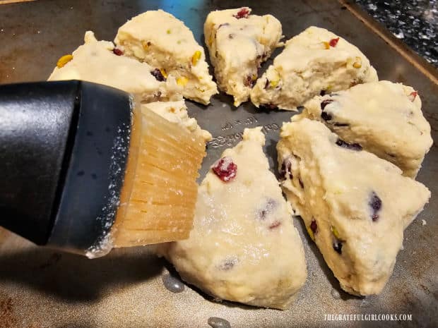 Scones are cut into wedges, then half and half is brushed on top of each one.
