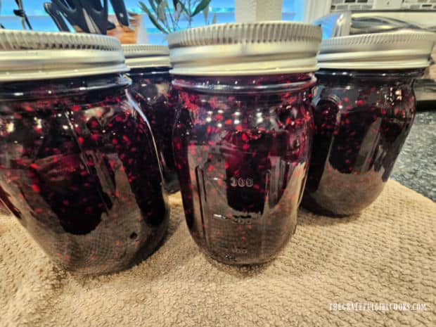 Jars of marionberry jam cool on a dish towel on the counter.