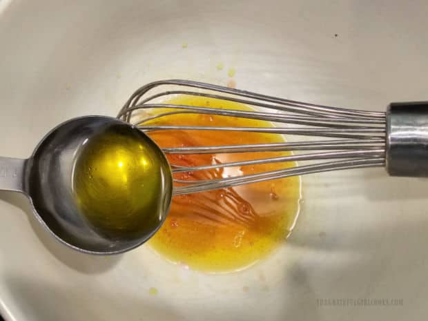 Olive oil is drizzled and whisked into olive oil and salt in a salad bowl.