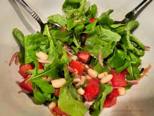 Baby arugula leaves are added to the panzanella salad and tossed to combine.