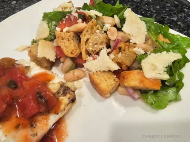 Thin slices of Parmesan are added to the panzanella salad on a plate with halibut.