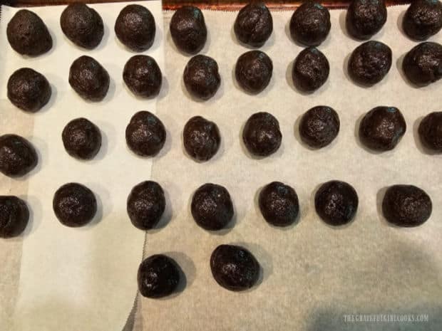Chocolate balls are placed on a parchment paper-lined baking sheet.
